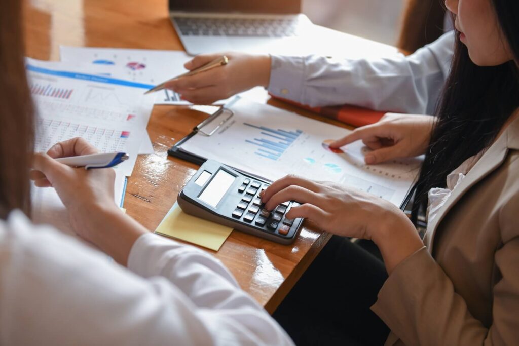 Close-up of hands calculating figures with calculator and documents.