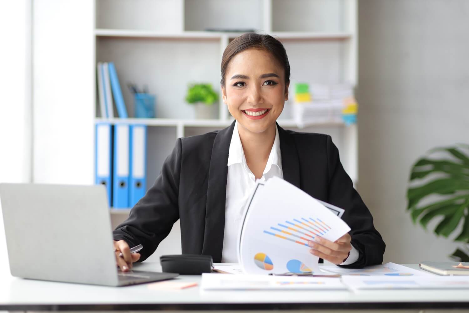 Smiling businesswoman holding financial charts inside a modern office