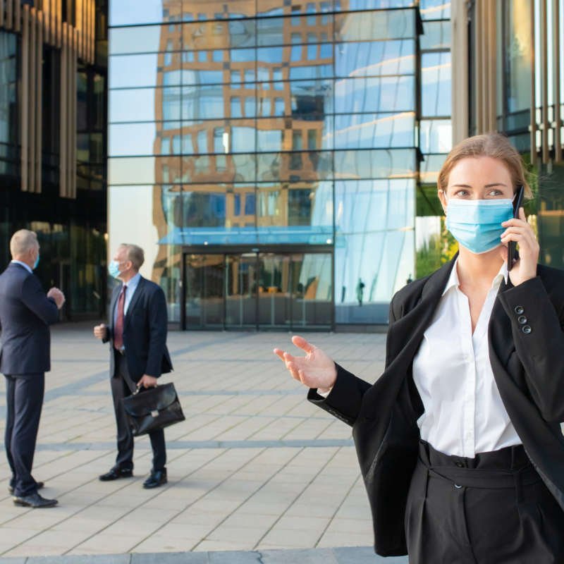 Businesswoman walking outdoors while checking phone near office buildings.