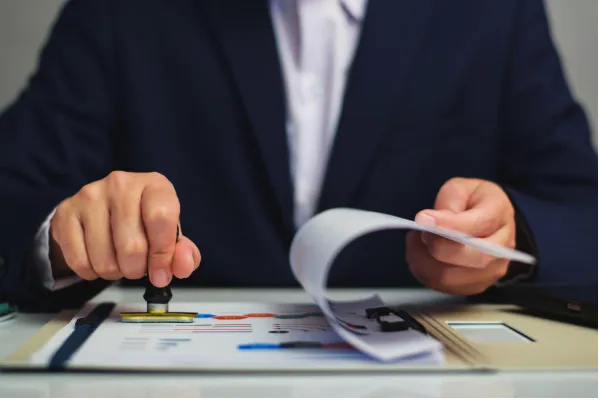 Office worker validating financial documents using a stamp and clipboard on a wooden workspace.