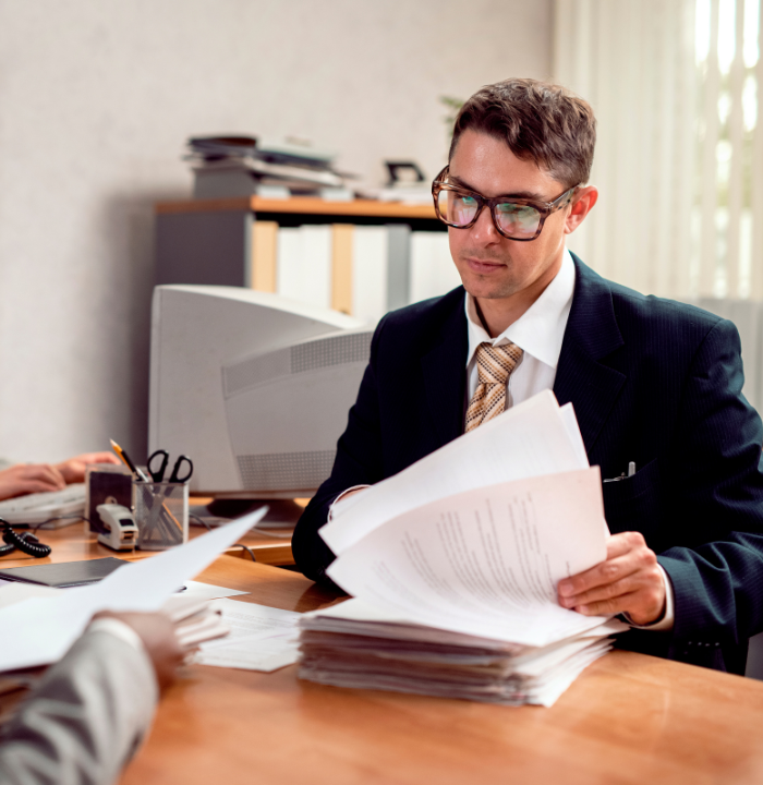 Business professional reviewing multiple documents at an office desk during a corporate compliance or accounting review.