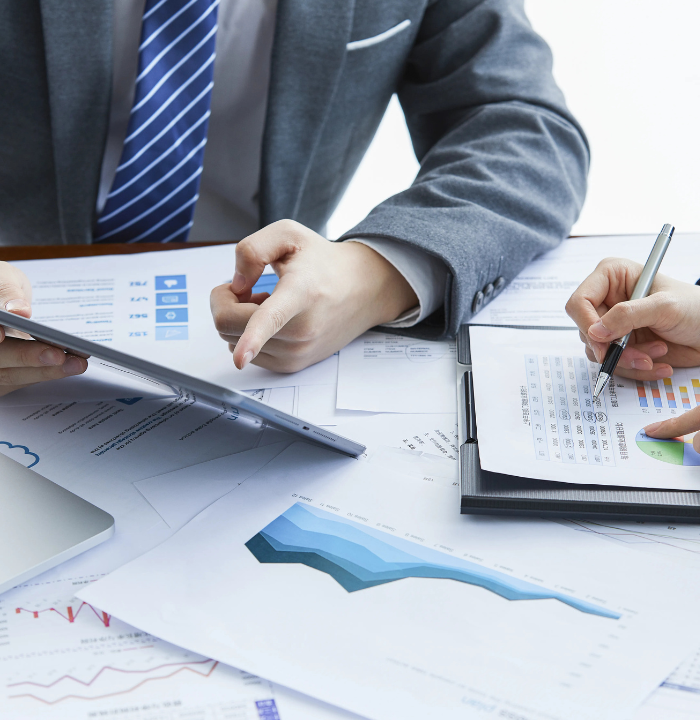 Close-up of hands discussing business figures with a tablet, printed reports, and data sheets on a desk.