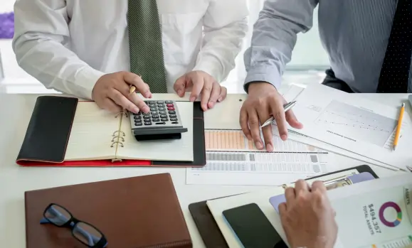 Two business professionals analyzing financial documents and using a calculator during a meeting, representing corporate tax calculations in the UAE.